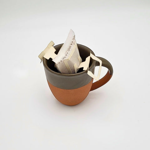 House of Nepal Jalpa Gold Drip Filter coffee bag in a two-tone ceramic mug, ready for brewing.