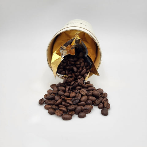 House of Nepal Jalpa Gold coffee beans spilling from a white paper tin with gold interior. 100% Arabica.