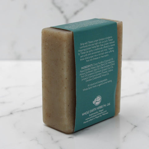 House of Nepal Tibetan Hotsprings Juniper Body Soap, a natural, beige bar with visible botanical flecks, wrapped in a teal label detailing ingredients and benefits.