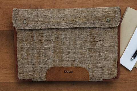 House of Nepal Kolpa 15-inch laptop sleeve made from natural nettle fiber and brown leather trim. Features a flap closure with metal snaps and a leather accent with the Kolpa logo.