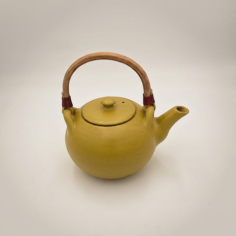 House of Nepal mustard yellow ceramic teapot with a natural wood handle and red twine accents. Round body, curved spout, and matching lid.