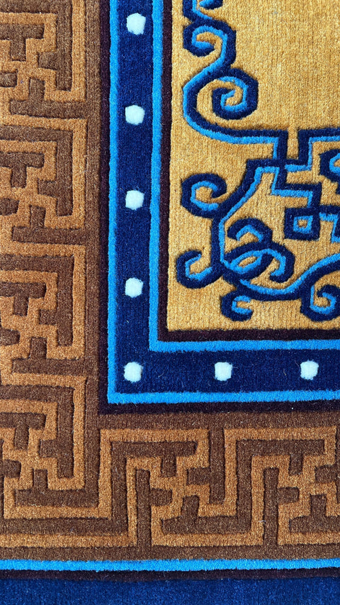 House of Nepal Teppich aus tibetischer Wolle in Ockergelb mit blauem Endknoten-Muster und geometrischem Rand