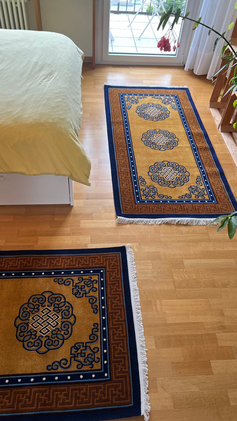 House of Nepal Teppich aus tibetischer Wolle in Ockergelb mit blau-weißen Ewigen Knoten und Fransen, 90x190 cm