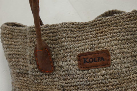 House of Nepal woven jute tote bag with brown leather handles and a leather logo patch.